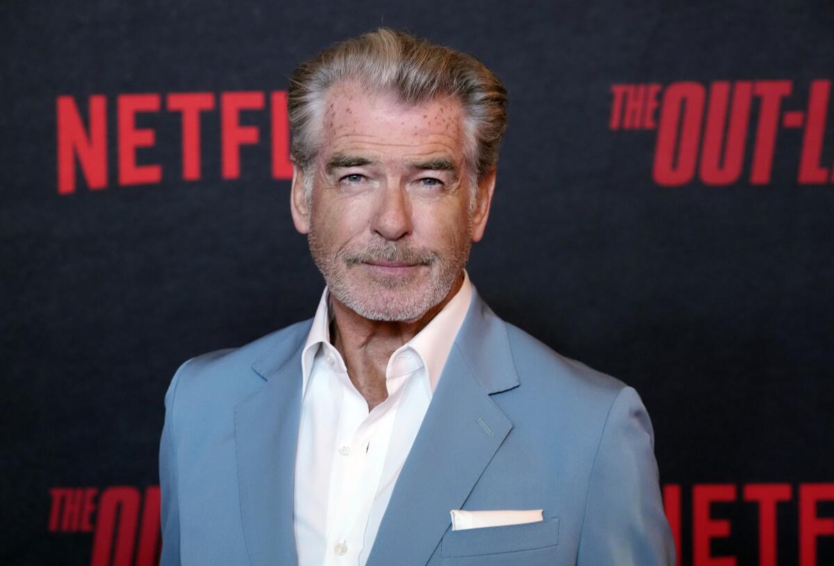 Pierce Brosnan wears a blue blazer and a white dress shirt as he poses for photos at a red carpet event.