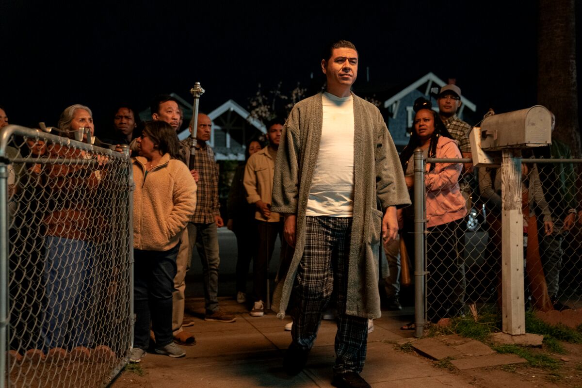 Julio in a bathrobe, white shirt and pajama pants, is walking through a gate at night.
