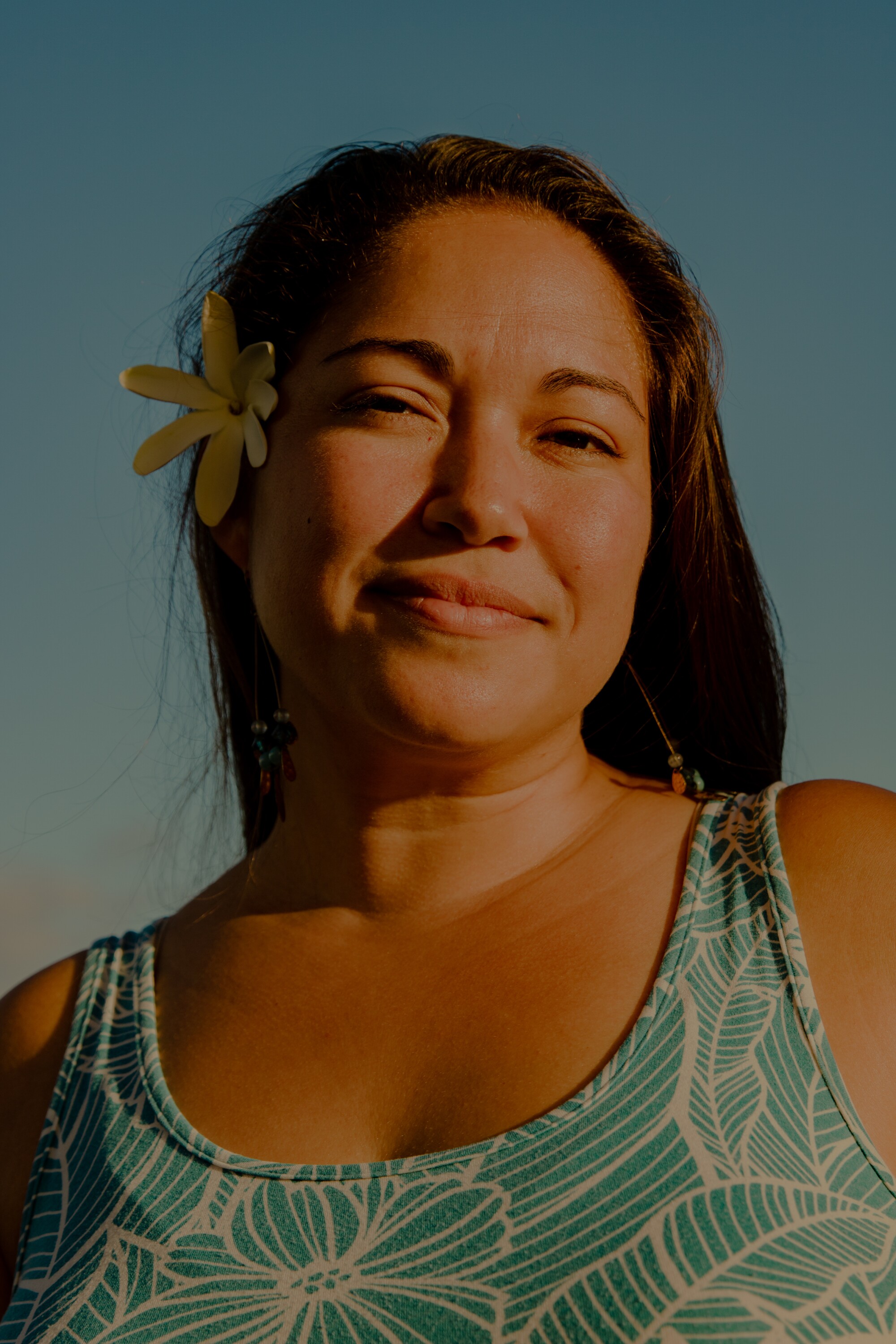 A woman posing in a blue patterned top with a yellow flower in her hair
