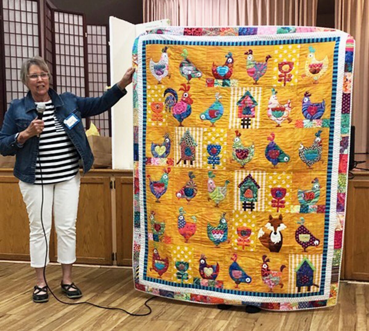 Carol Simpson talking about a chicken-themed quilt during a Seaside Quilter Guild meeting’s “Show and Tell” time.
