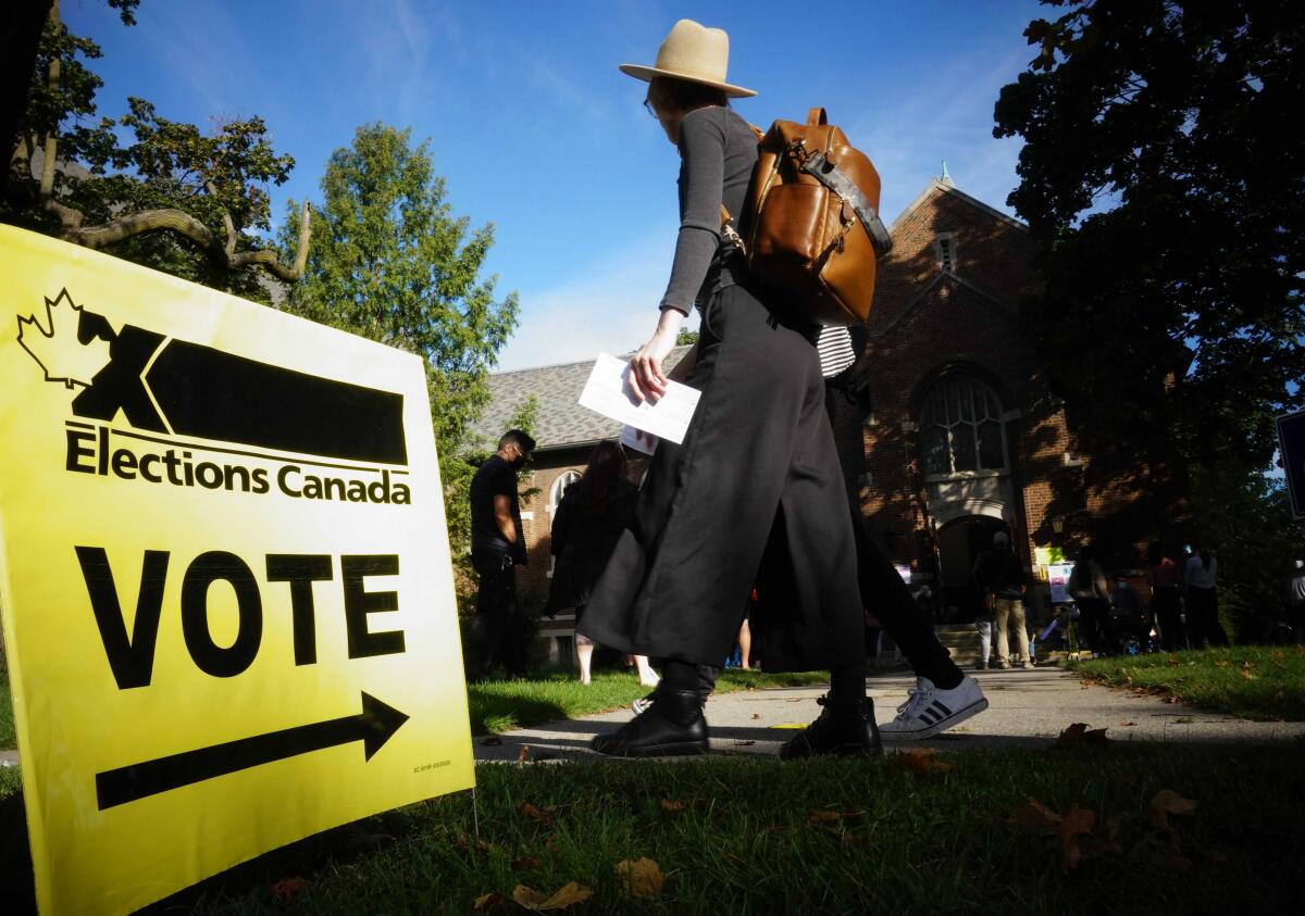 People walk past a lawn sign that says Elections Canada, Vote
