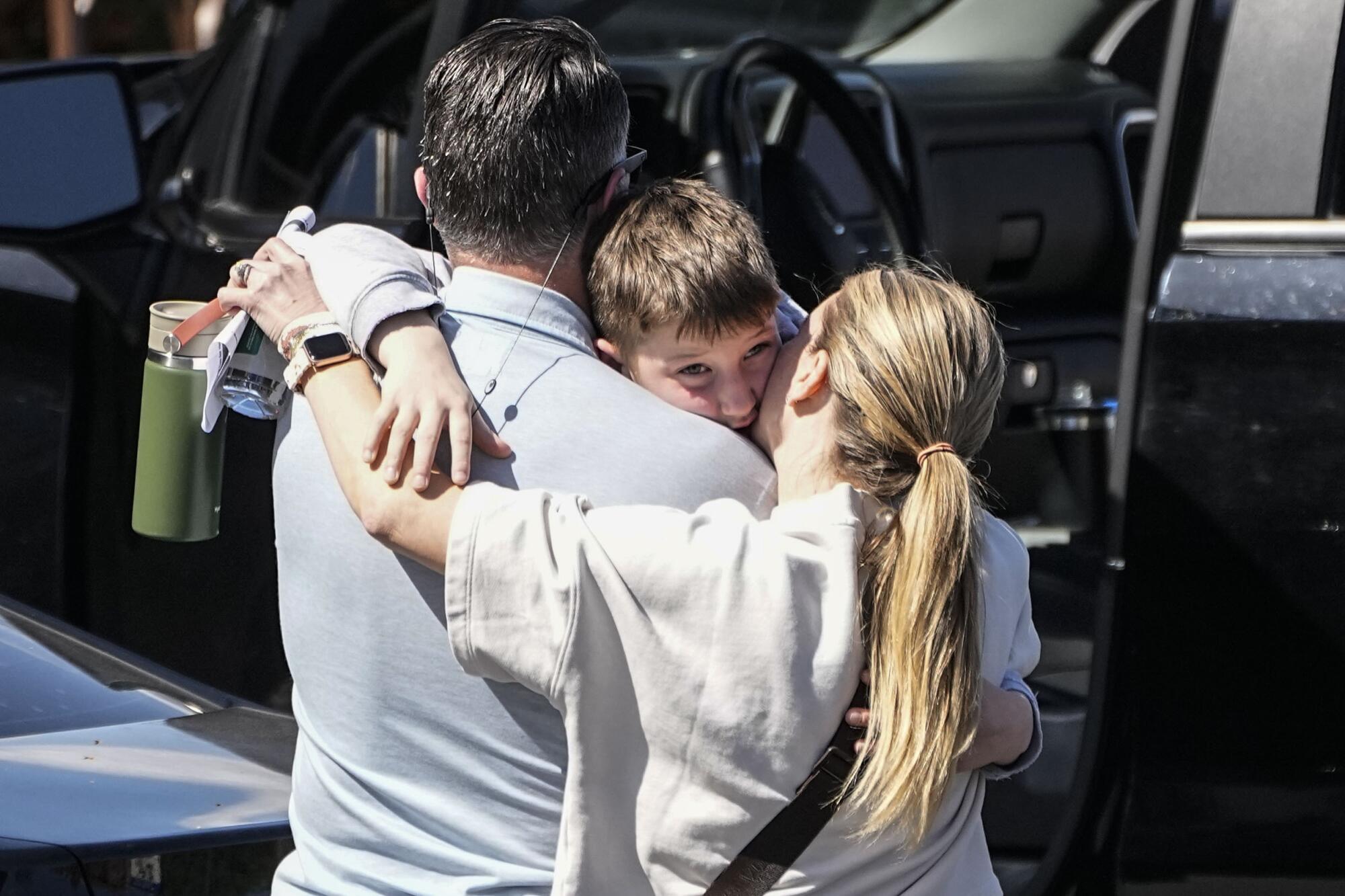 A man and woman stand with their arms around a child.