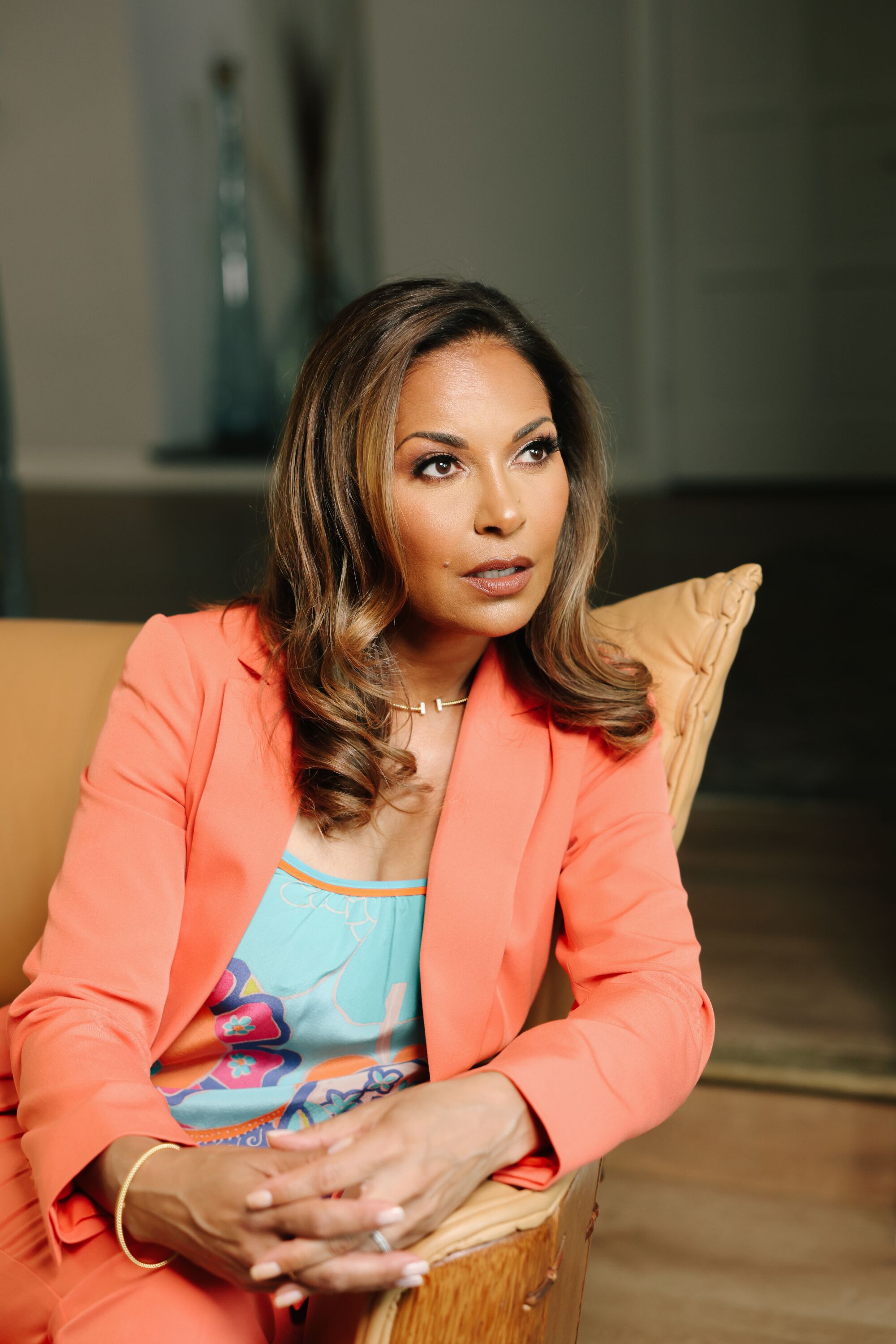 A woman in an orange suit poses in her home