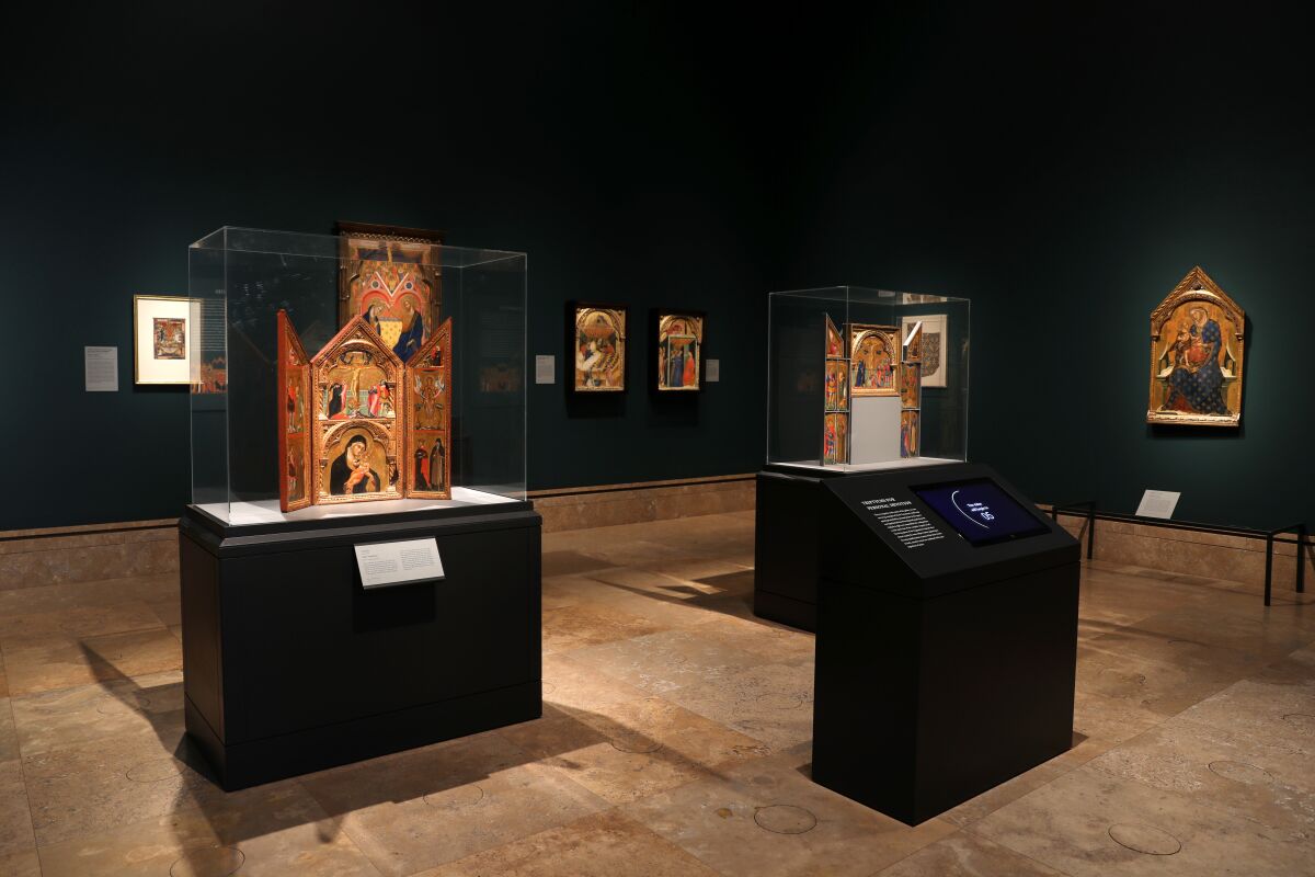 An installation view of glowing altarpieces in a dark-walled gallery.