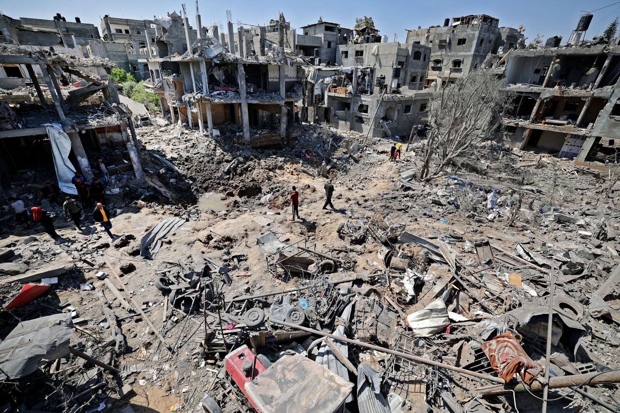 A few people walk amid the rubble of flattened and severely damaged buildings.