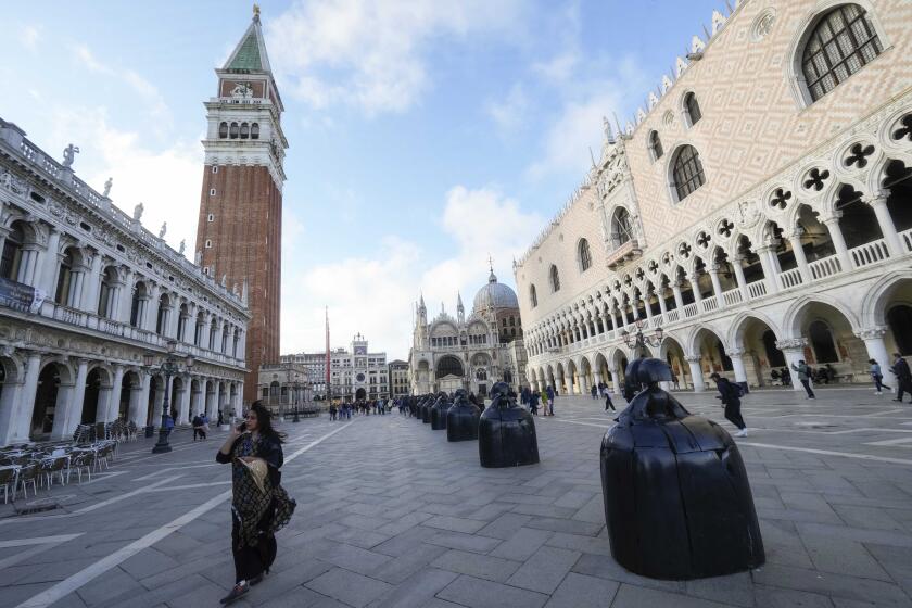 A visitor walks next to the 'Las Meninas a San Marco' sculptures part of the installation by the Spanish artist Manolo Valdés, at the San Marco's Square during the 60th Biennale of Arts exhibition in Venice, Italy, Tuesday, April 16, 2024. The Venice Biennale contemporary art exhibition opens Saturday for its six-month run through Nov. 26. The main show titled 'Stranieri Ovunque – Foreigners Everywhere' is curated for the first time by a Latin American, Brazilian Adrian Pedrosa. Pedrosa is putting a focus on underrepresented artists from the global south, along with gay and Indigenous artists. Alongside the main exhibition, 88 national pavilions fan out from the traditional venue in Venice's Giardini, to the Arsenale and other locations scattered throughout the lagoon city. (AP Photo/Luca Bruno)