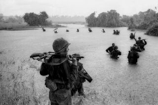 Paratroopers of the U.S. 2nd Battalion, 173rd Airborne Brigade hold their automatic weapons above water as they cross a river in the rain