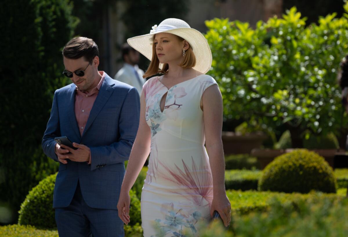 A man in a blue suit and a woman in a floral dress walk the grounds of a Tuscan villa
