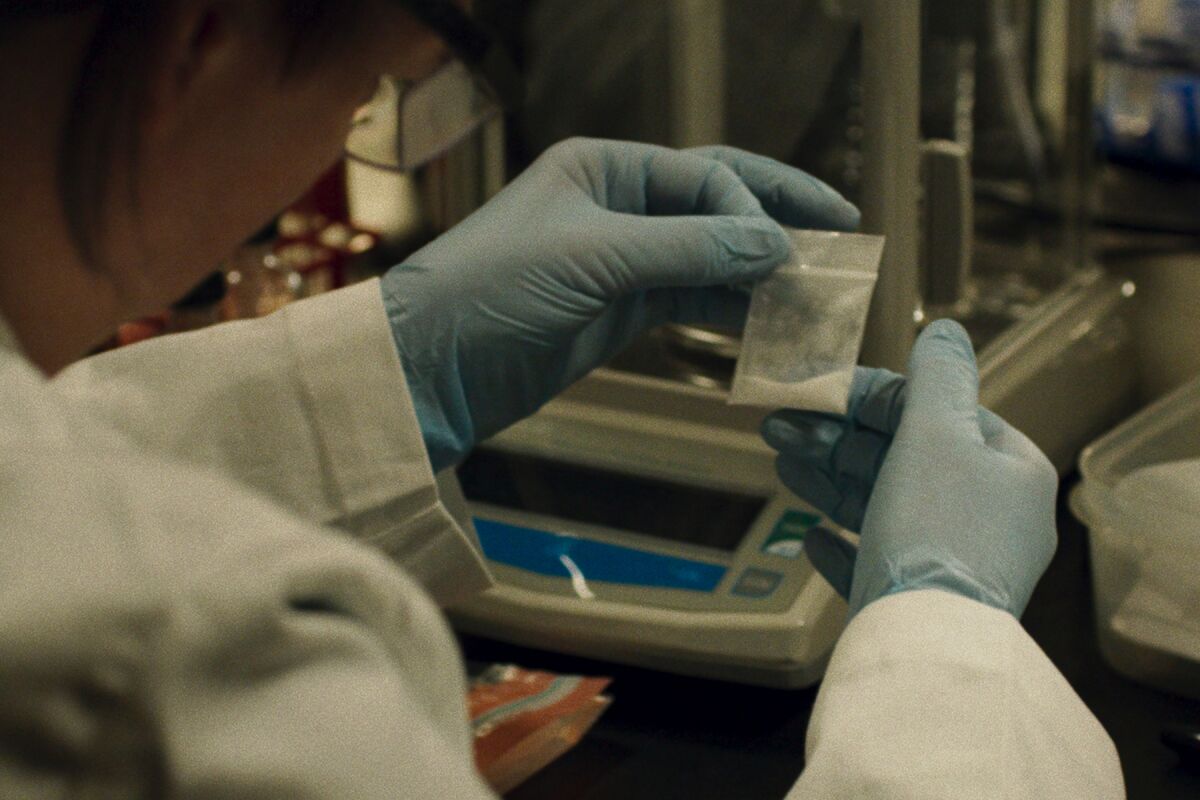 A lab technician holds a small bag containing white powder in "How to Fix a Drug Scandal” on Netflix.