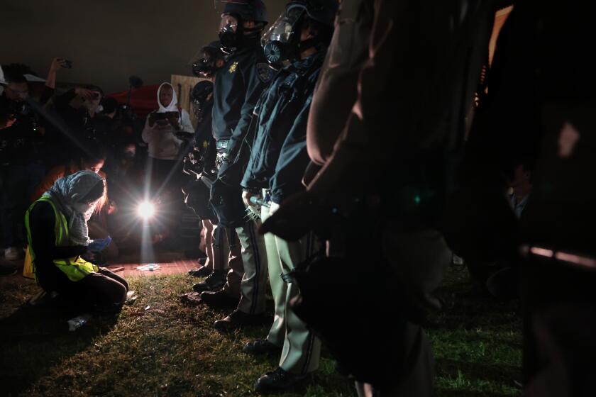 LOS ANGELES, CALIFORNIA - May 1: A woman prays in front of CHP officers next tot he pro-Palestinian encampment at UCLA early Wednesday morning. (Wally Skalij/Los Angeles Times)