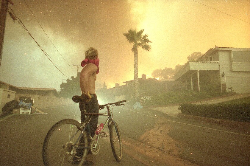 A man on a bike watches as flying embers and flames land on the street during the Laguna fire in October 1993.