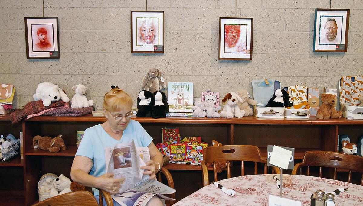 Phyllis Nasella, of Glendale, reads the newspaper near where a portrait of Marilyn Monroe, second from left, and others works by La Crescenta artist William Woeger, are now on display at Penelope's Cafe Books and Gallery until October, in La Cañada Flintridge on Tuesday, August 25, 2015.