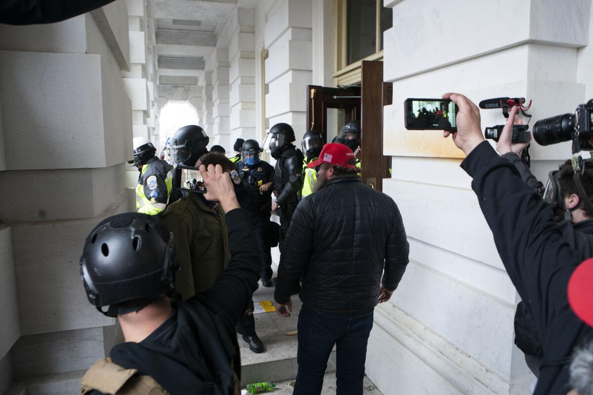 People raise smartphones and cameras as figures approach Capitol police officers.