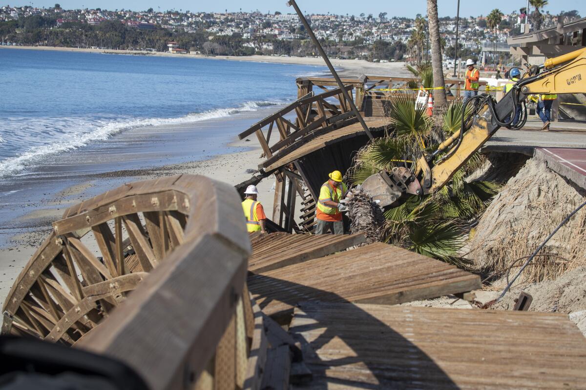 People in orange T-shirts and yellow vests work on wood planks next to a beach.