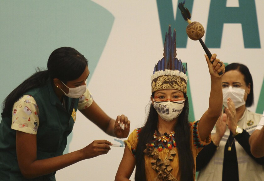 A woman uses a syringe to administer a shot to a woman in Indigenous dress.
