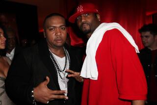 Timbaland wearing black cardigan and white shirt poses with Magoo who is wearing an oversized red t-shirt and red cap