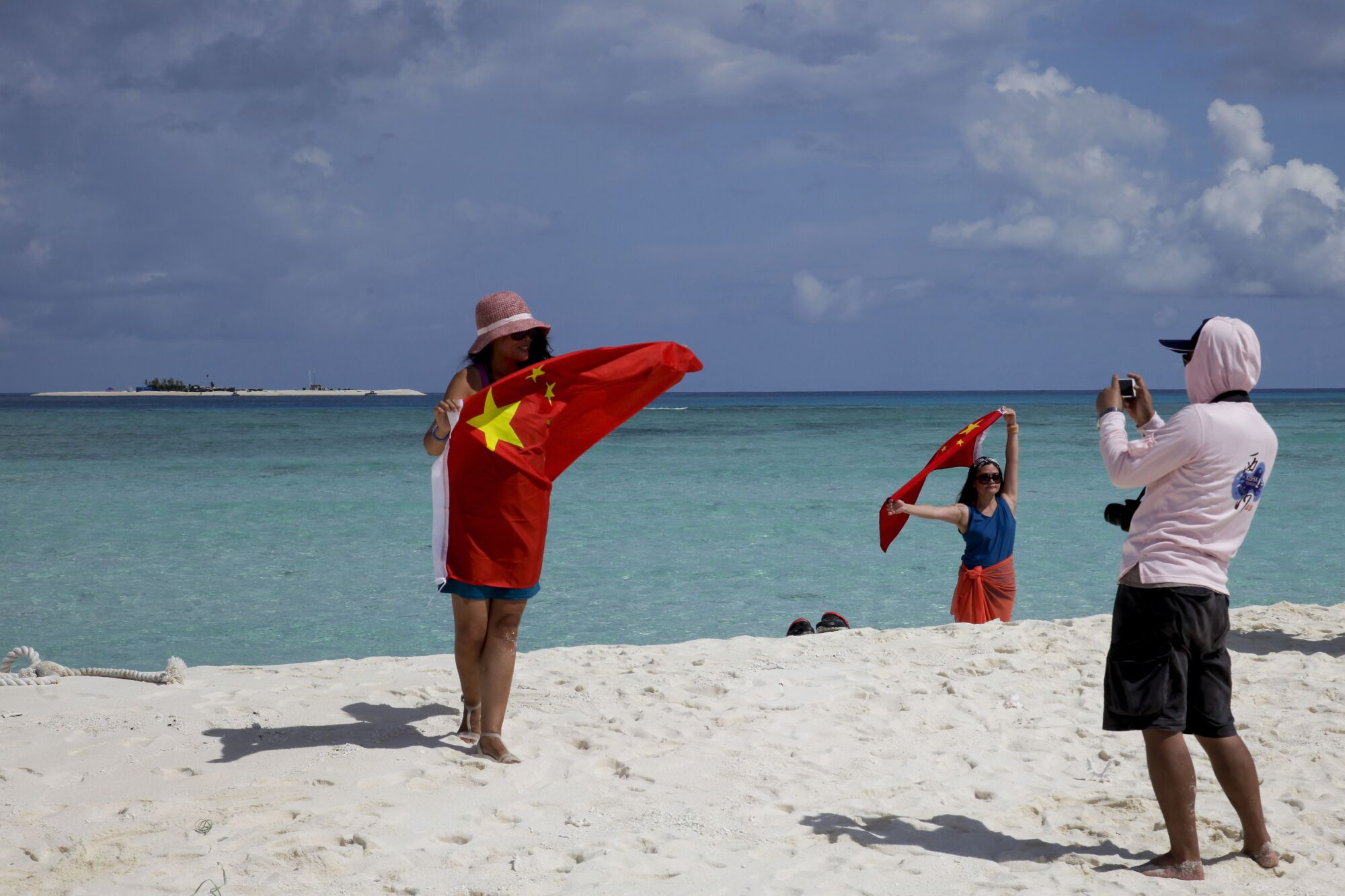 People hold the red Chinese flag on a white-sand beach