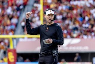 USC coach Lincoln Riley signals up field while holding a card that contains the Trojans' offensive plays 