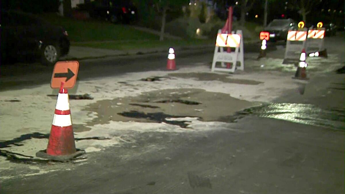 Sand covers seeping tar, blocked off by cones, on a road.