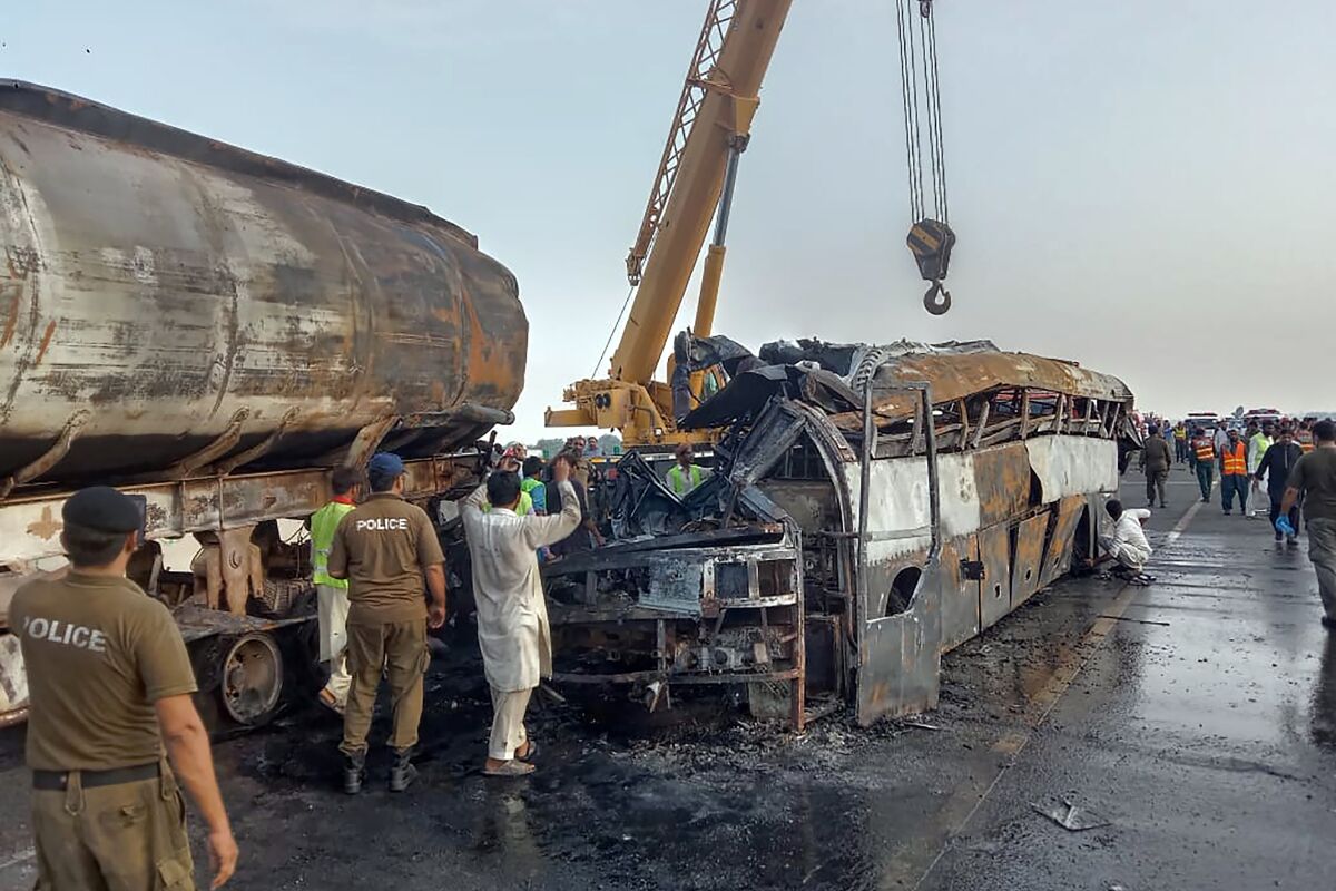 Agentes de policía y trabajadores retiran los restos de un autobús que chocó con un camión cisterna en una autopista en Uch Sharif, cerca de Multan, Pakistán, el martes 16 de agosto de 2022. (AP Foto)