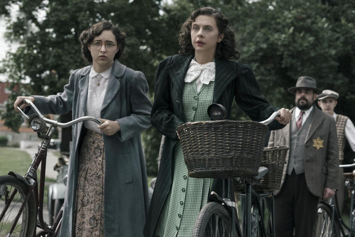 Two young women in 1940s clothing walk their bicycles in a scene from "A Small Light"