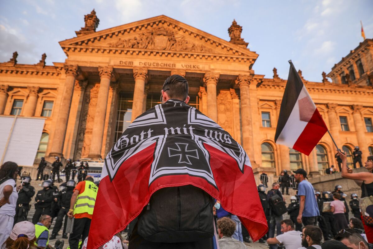 A person wrapped in an iron cross flag in a crowd at the columned  Reichstag building   