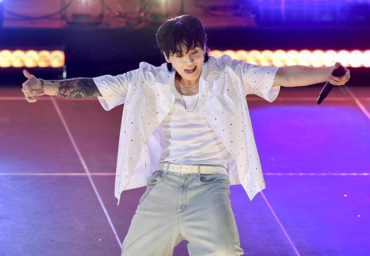 Jungkook of BTS wears a white shirt and jeans onstage and holds out his arms.