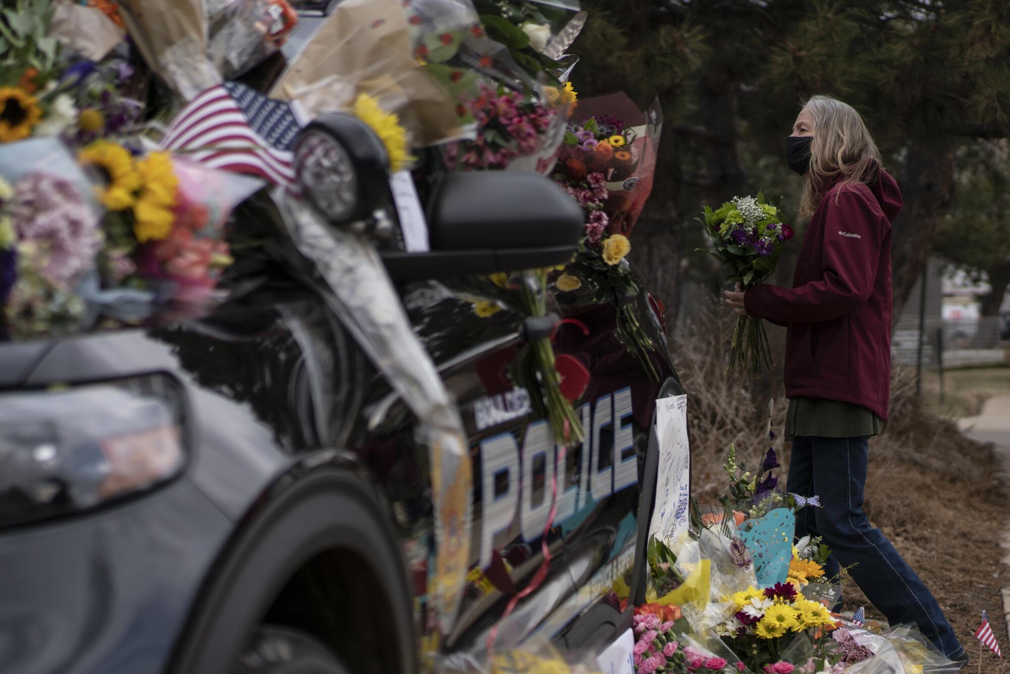 A woman adds a bouquet to a police cruiser covered with  flowers in memory of Boulder police Officer Eric Talley 