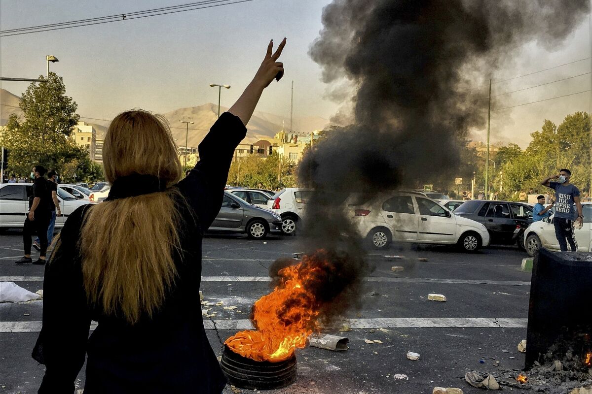 A woman holds her hand in the air as a tire burns in the street.