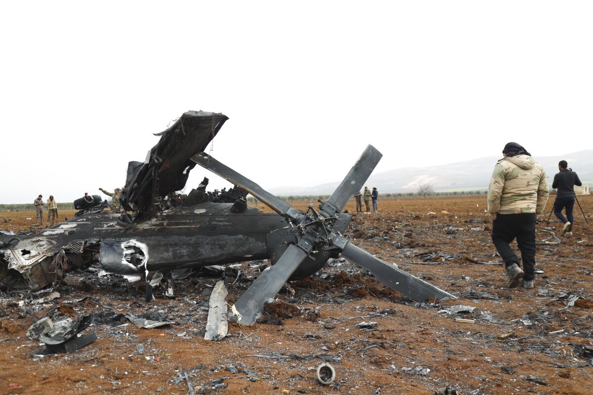 The wreckage of a helicopter is seen on a barren landscape