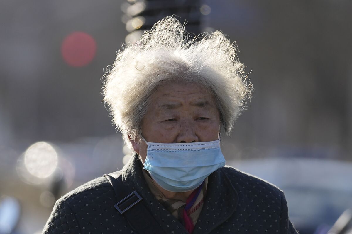 FILE - An elderly woman wearing a mask walks on a street of Beijing, China, Tuesday, Dec. 7, 2021. (AP Photo/Ng Han Guan, File)