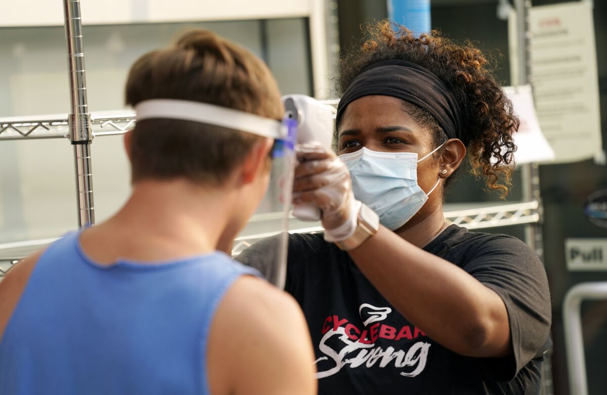 CycleBar employee Nia Freeman takes the temperature of a cyclist before a fitness class in Culver City.