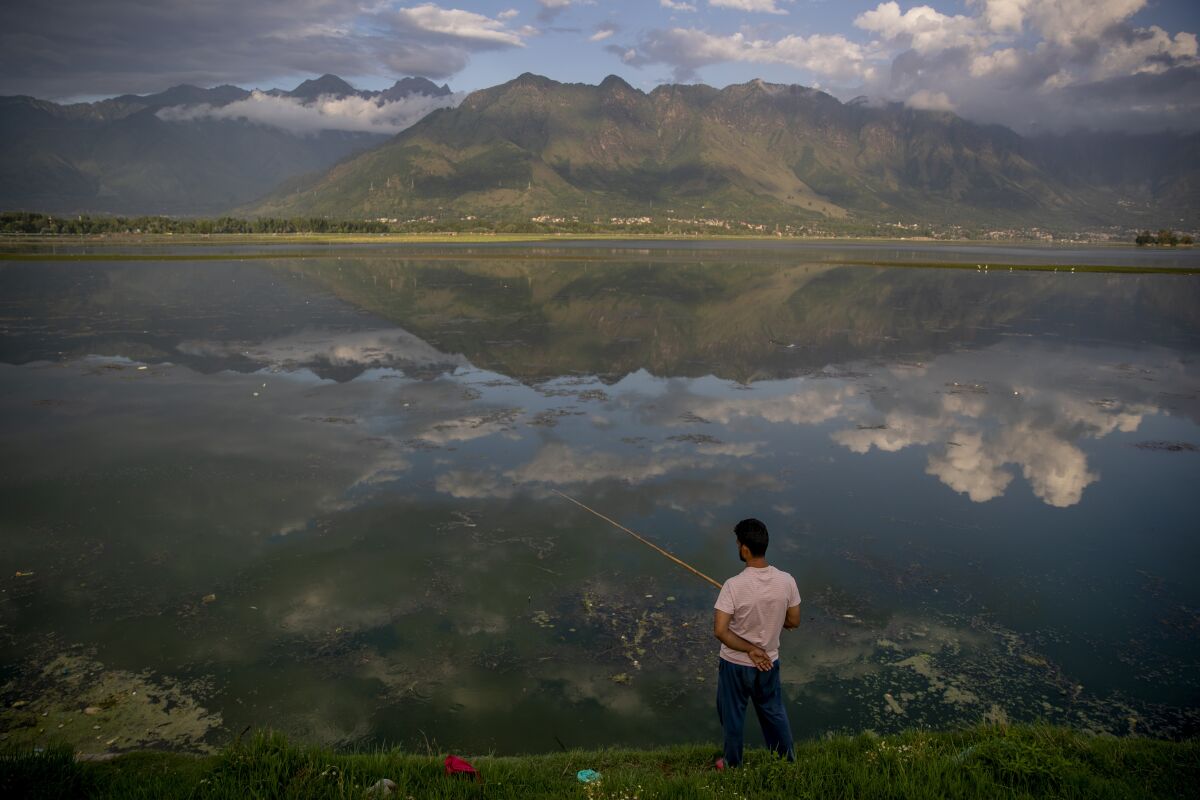 Clouds are reflected in water as a Kashmiri man fishes in the Dal Lake on the outskirts of Srinagar, Indian controlled Kashmir, Friday, July 30, 2021. (AP Photo/Dar Yasin)