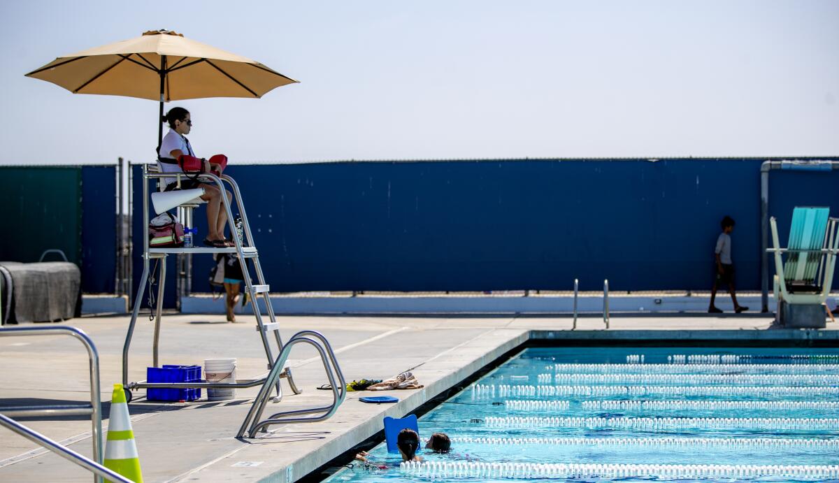 A lifeguard sits in a tower under an umbrella at the foot of a public pool