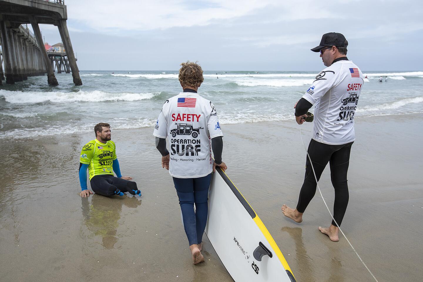 Caleb Brewer, left, of the U.S. Army, prepares to go out in the surf with assistance from volunteers Pops, center, and Jeff Porhaska, right, during the 2nd Annual Operation Surf in Huntington Beach on Monday , June 4.