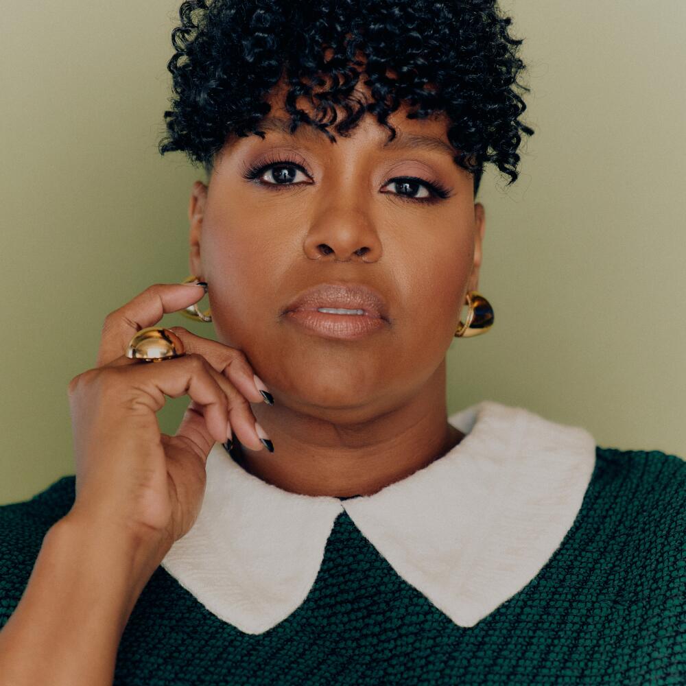 A woman, wearing a black blouse with a white collar, holds her right hand to her cheek