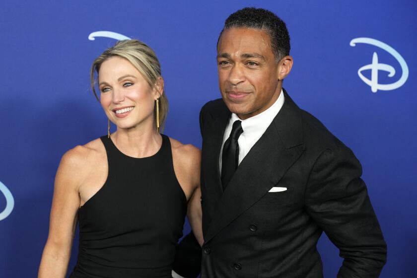 A woman in a black dress and a man in a dark suit pose at a red-carpet event