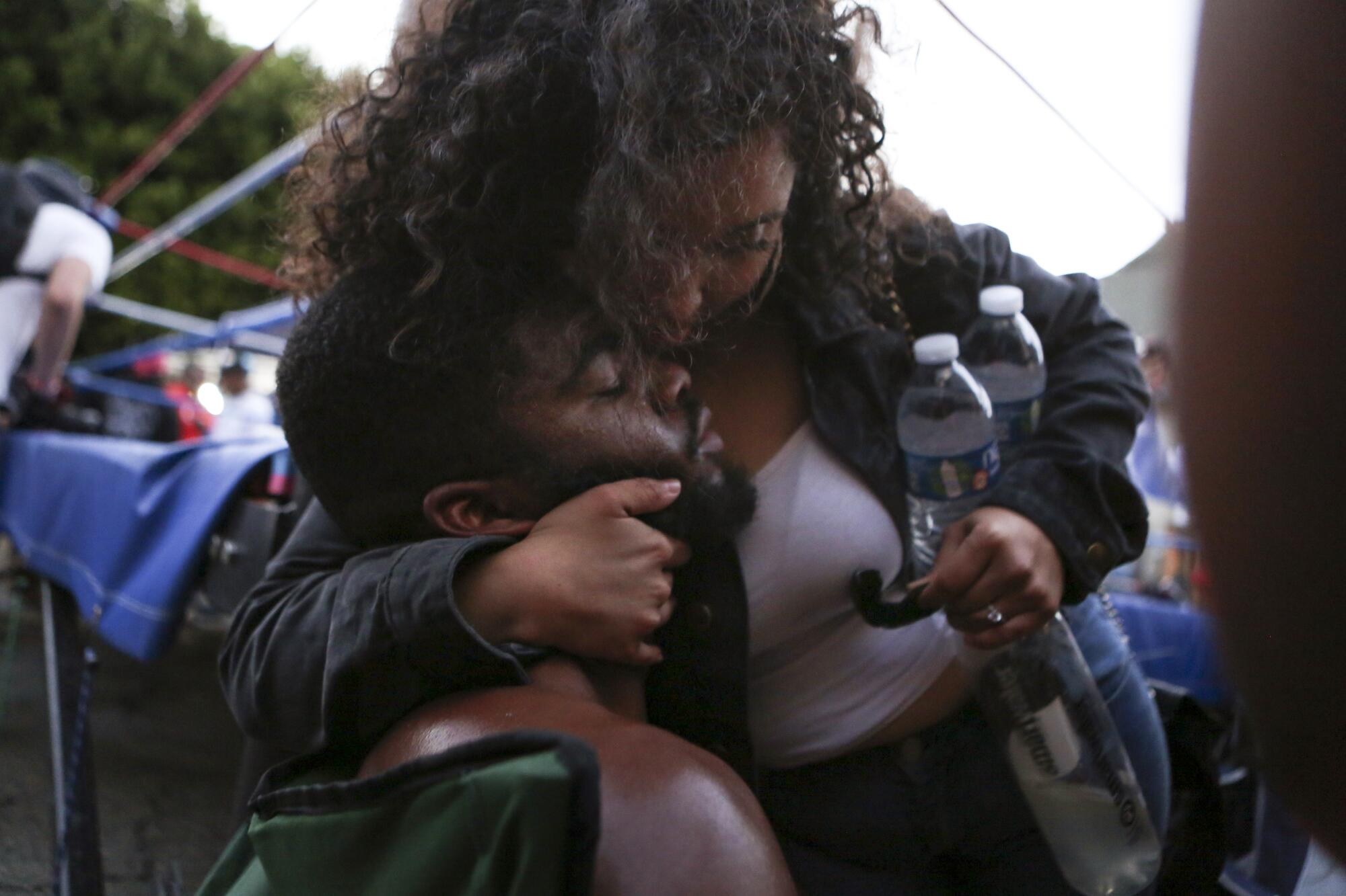 A woman holding two water bottles in one arm puts her other arm around a man's neck for a close hug.