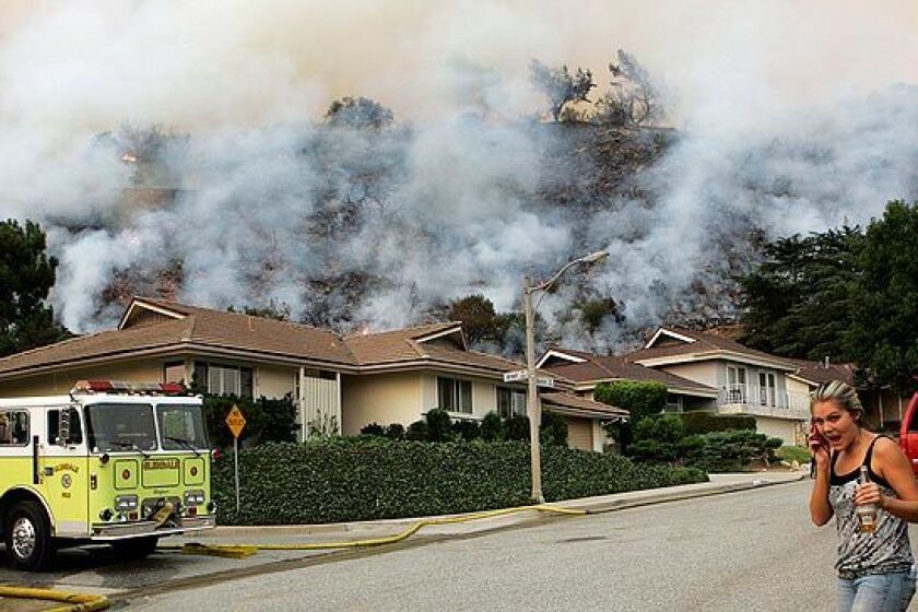 A resident talks on her cellphone as a smoky hillside looms behind homes on Boston Avenue in La Crescenta on Tuesday.