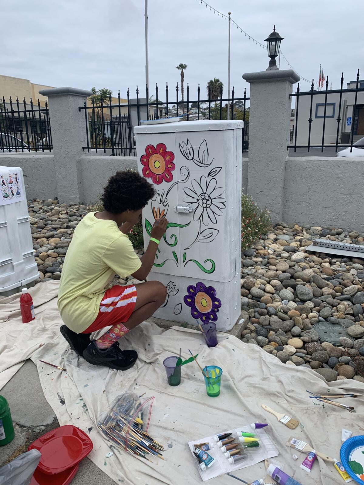 A Warren-Walker middle school student fills in floral designs on a utility box outside the UPSES Hall in Point Loma.