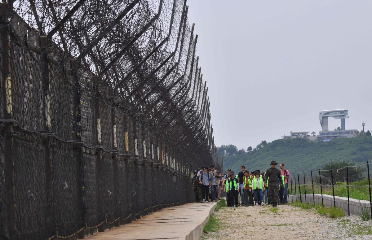 Hikers walk along a fence in the DMZ. Atop a hill is a South Korean observatory tower.