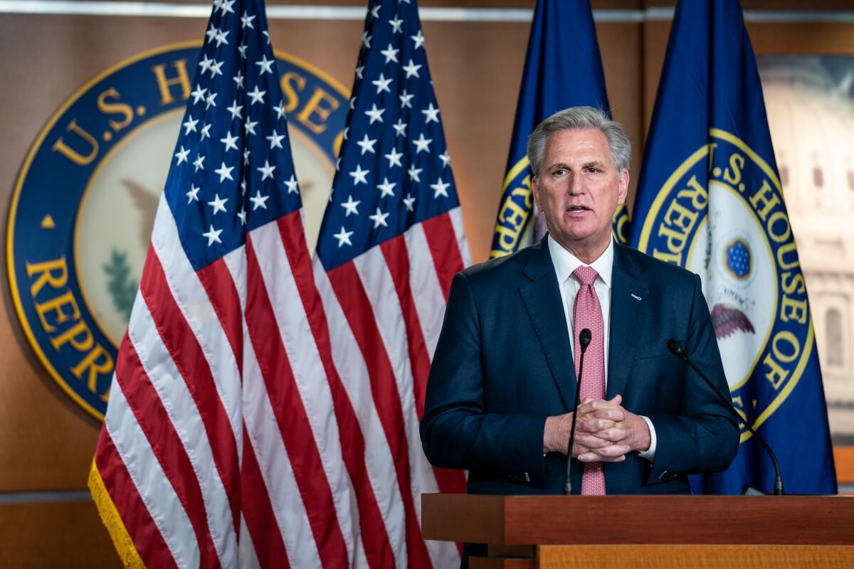 A man speaks at a lectern with U.S. and House flags behind him.