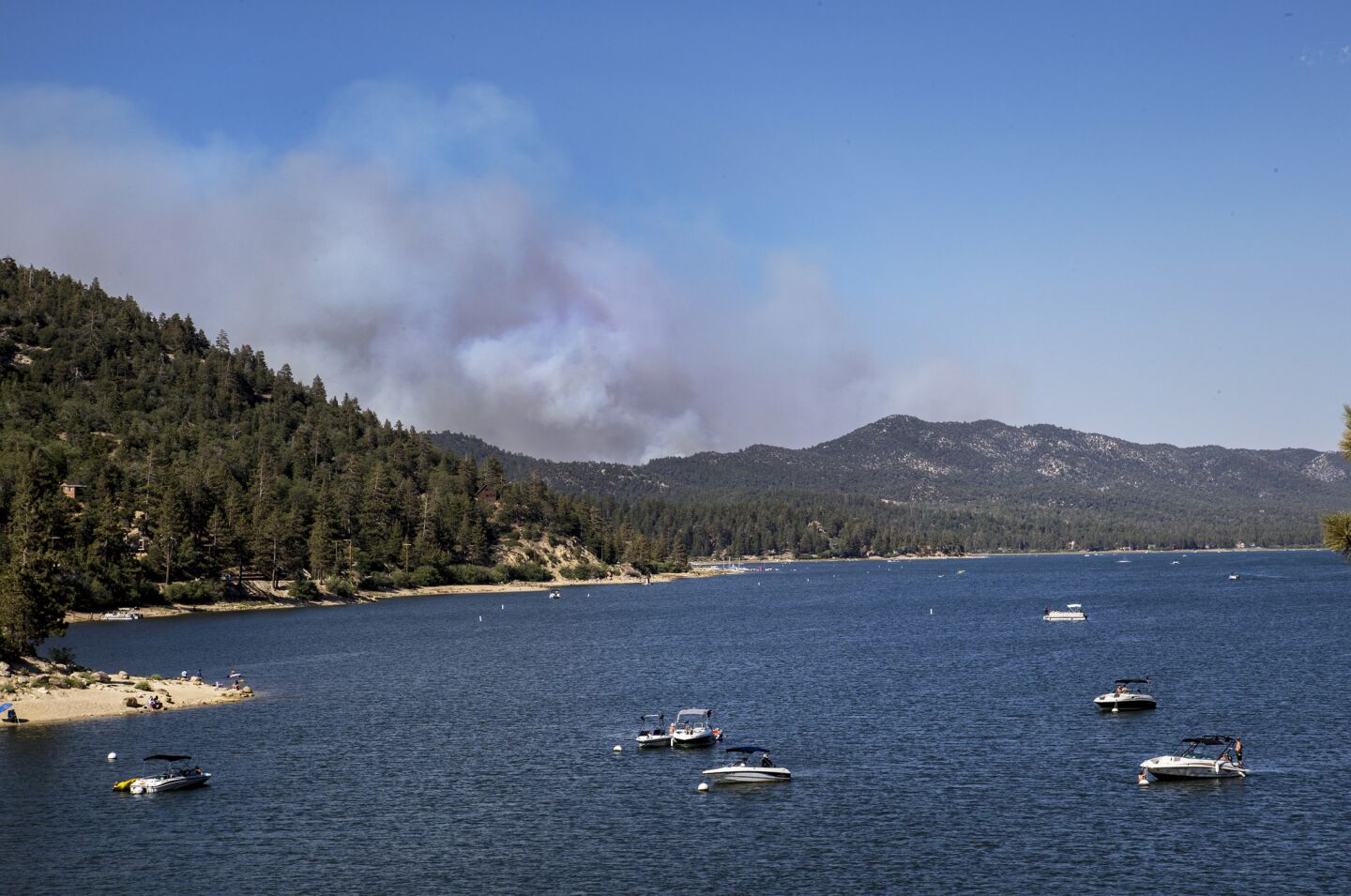 Boaters relax on Big Bear Lake as a giant plume from the Holcomb fire burns nearby in rugged terrain in the San Bernardino National Forest.