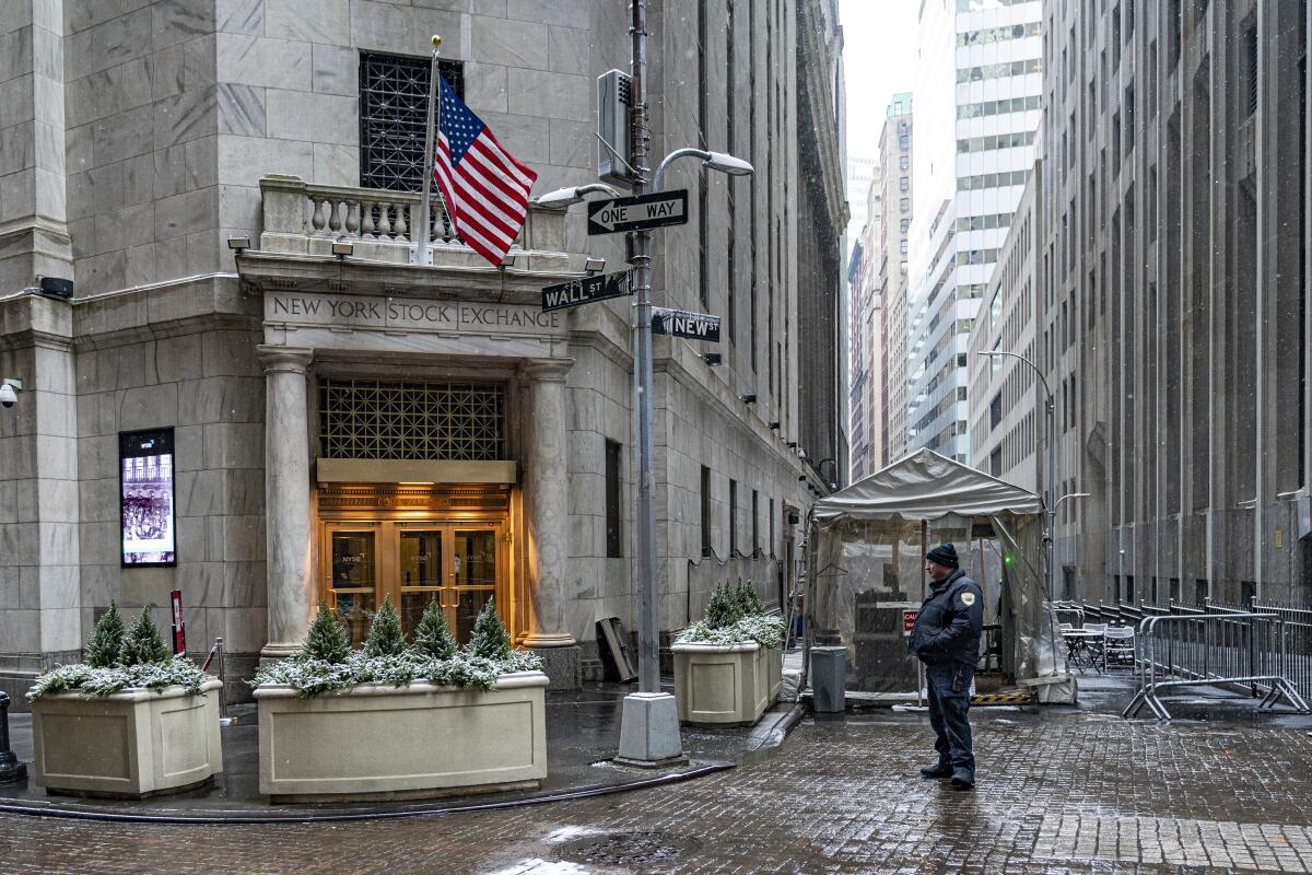 A person stands outside an entrance to the New York Stock Exchange, which has an American flag hanging from it.