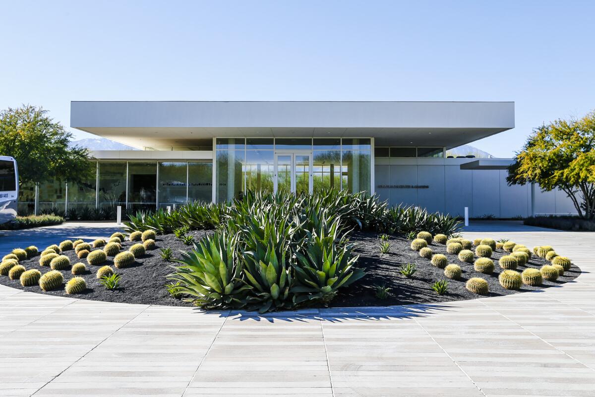 Exterior view of a flat-roofed, glass-fronted modernist building with succulents and cactus in front