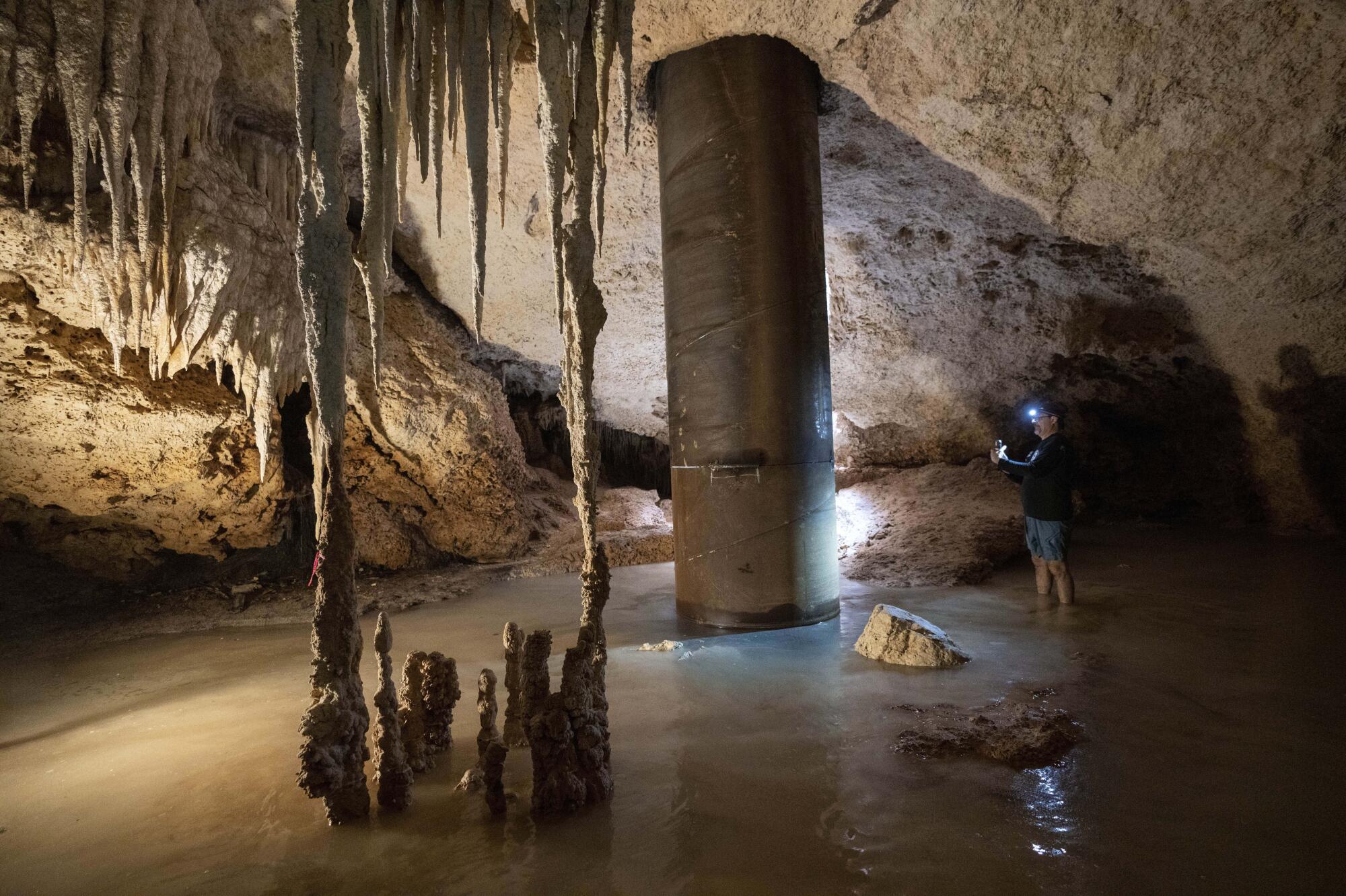 Ein Mann fotografiert einen künstlichen Pfahl, der durch die Decke einer Höhle ins darunter liegende Wasser verläuft.