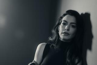 Anne Hathaway sits and leans against a wall in a black-and-white portrait