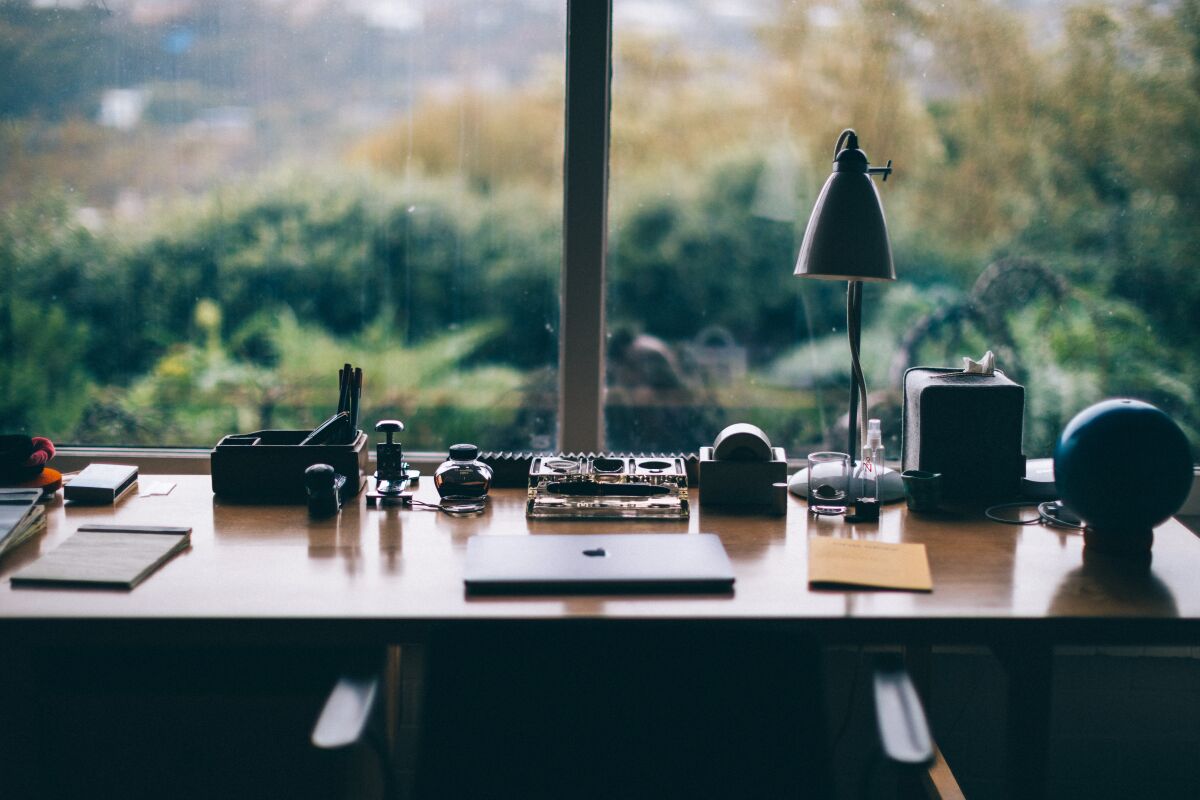 A desk with a laptop and a view from the windows to the greenery outside.