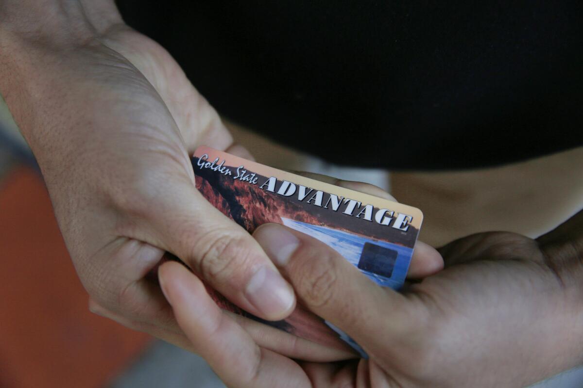 A person's hands hold a California EBT card
