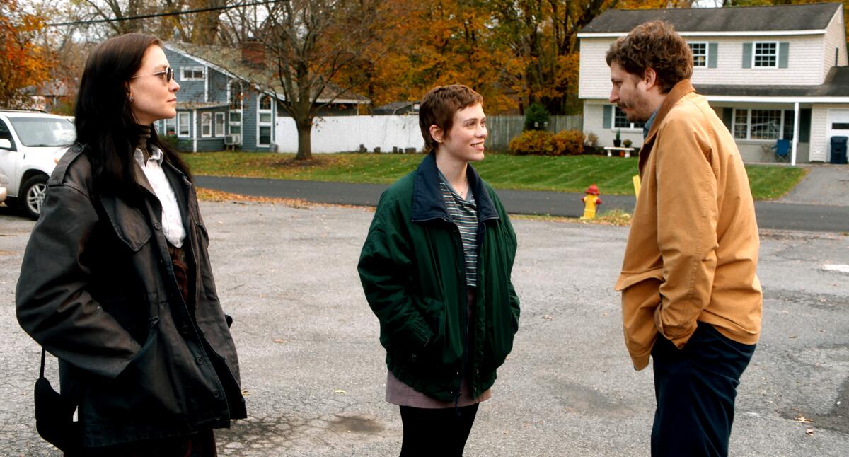 Two women and a man have a conversation outdoors, on a suburban street.